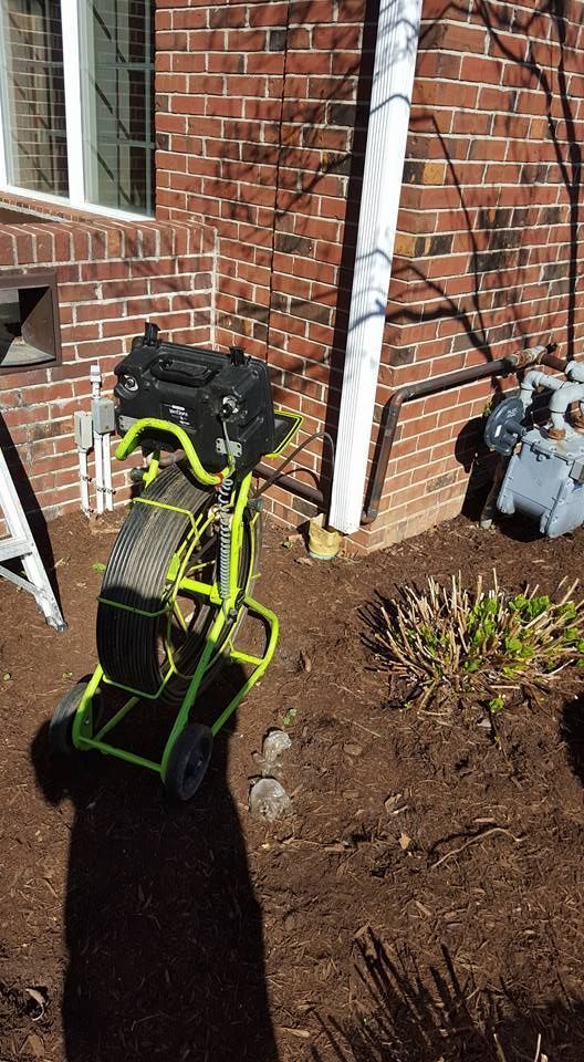 Green and black drain cleaning machine near a brick building.