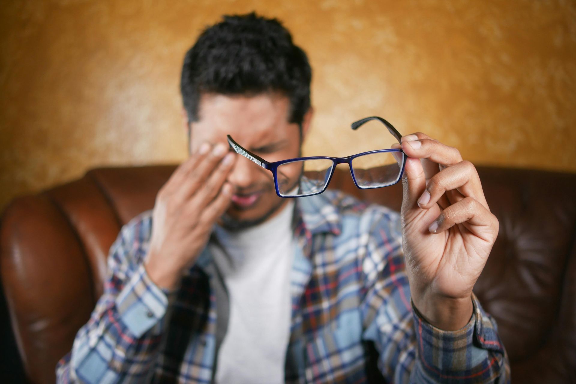 A man is sitting on a couch holding a pair of glasses.