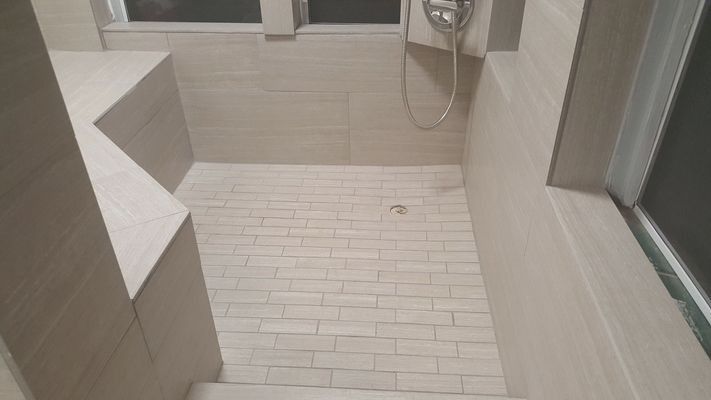 Tiled shower with beige brick floor, beige walls, and a shower head.
