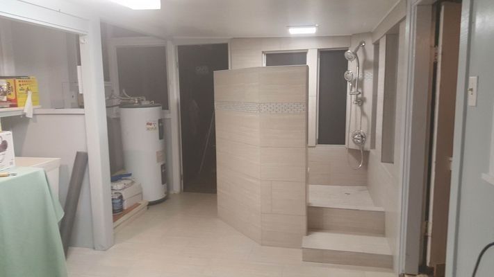 A small bathroom with a shower, water heater, and a partially open door. Beige and white tones.