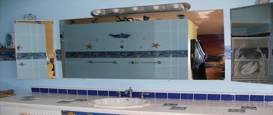 Bathroom vanity with blue tiled walls, sink, mirror, and cabinets decorated with seashells.