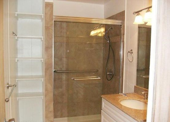 Bathroom with glass shower, sink, and shelves. Beige and white tones.