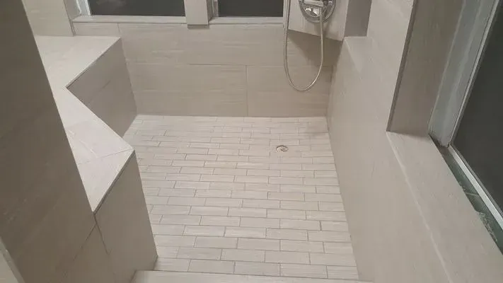 A shower with light-colored tile floor and walls, a built-in bench, and showerhead.