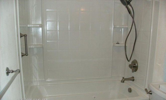 White bathroom with tub, shower head, and grab bar.