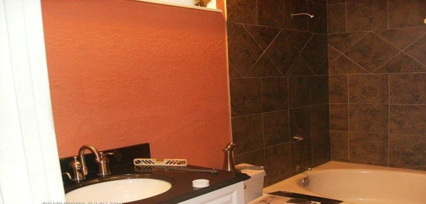 Bathroom with orange wall, black countertop with sink, and dark tiled shower/tub.