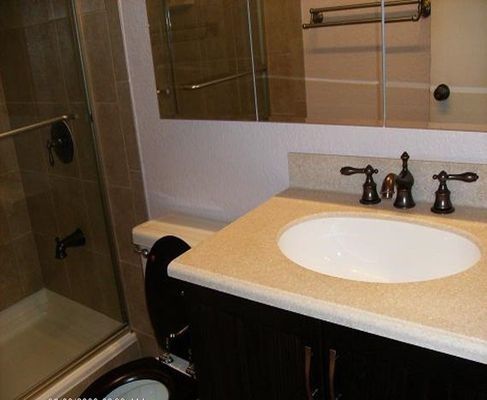 Bathroom with sink, toilet, shower, and mirror. Brown cabinets, beige countertop, and light brown tile.