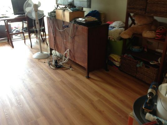 A cluttered room with wooden floors, a fan, and furniture; wires are visible.