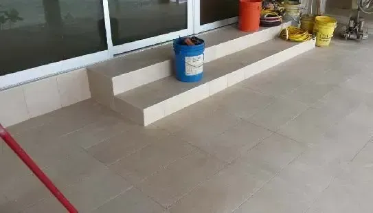 Exterior view of a building with light-colored tile and steps; a blue bucket sits on the steps.