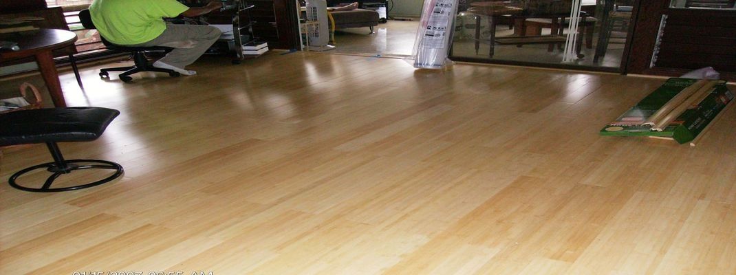 A person in a green shirt sits near a black stool, with laminate flooring.
