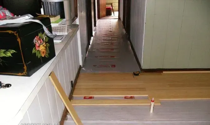 Hallway with new wood flooring being installed, light wood planks, beige underlayment.