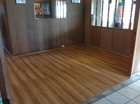 A room with wood paneling and wood-look flooring. Natural light streams in from windows.