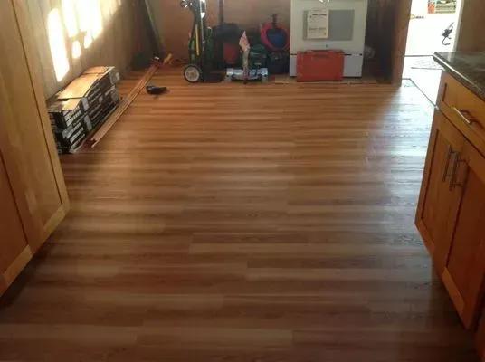 Hardwood floor in a kitchen with wooden cabinets on the sides, tools and other items are in the back.