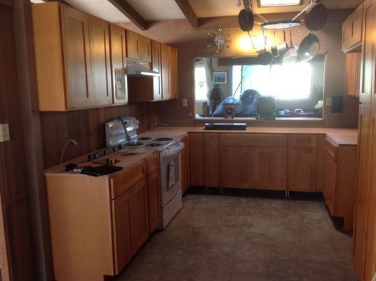 A kitchen with light wood cabinets, appliances, a window, and a wood-paneled wall.