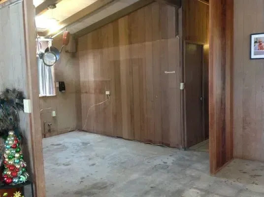 Room with wood-paneled walls and a concrete floor. A doorway, door, and festive décor are also visible.