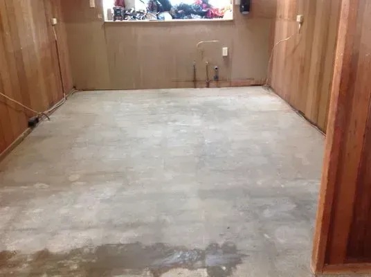 Concrete basement floor with wood paneling walls and exposed plumbing.