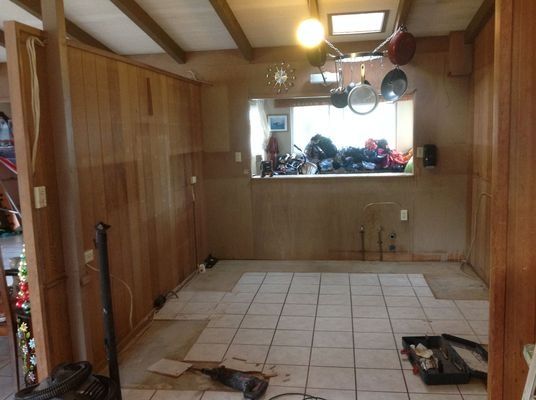 Interior of a room under renovation. Paneling on the walls, tiled floor, window, and pots hanging.