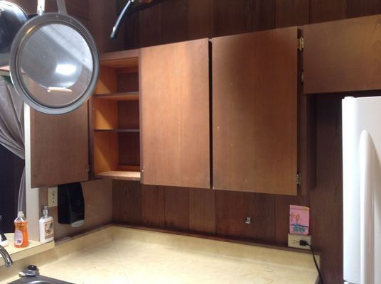 Kitchen cabinets, some open, above a countertop. Brown wood cabinets and paneling.