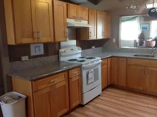 A kitchen with light wood cabinets, gray countertops, and a white stove.
