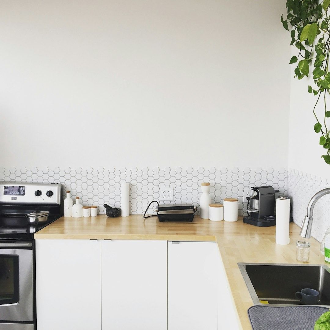 Modern white kitchen with a stainless steel stove, wooden countertops, and hexagon tile backsplash.