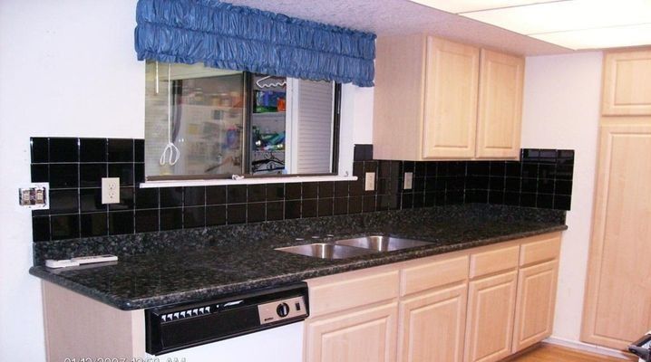 Kitchen with black tile backsplash, granite countertop, light cabinets, and a blue window treatment.