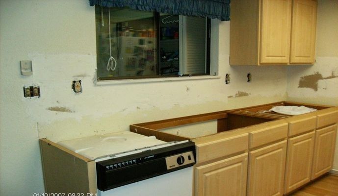 Kitchen undergoing renovation: cabinets installed, walls exposed, window, dishwasher.