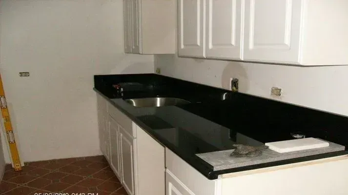 White cabinets and black countertop in a kitchen. A stainless steel sink and a tile floor.