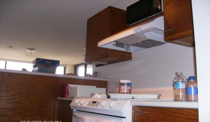 Kitchen with brown cabinets, white stove and countertop, microwave, and range hood.