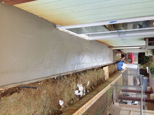 Person smoothing wet concrete; long, narrow construction area beside a building, with window and wood trim.