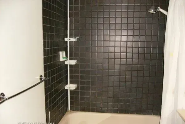 Dark tiled shower with a white curtain, grab bar, and shelf organizer.
