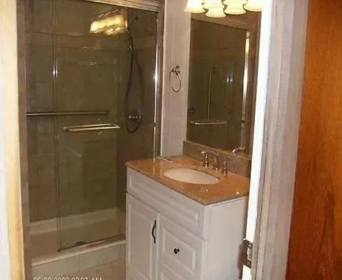 Bathroom with white vanity, tan countertop, glass shower, and mirror.
