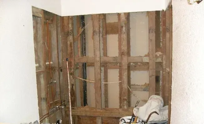 Bathroom wall under construction, exposed wood frame, pipes, and electrical wiring.