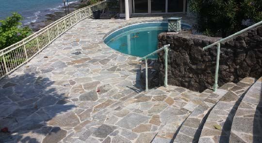 Stone patio with a curved pool, steps, and ocean view.