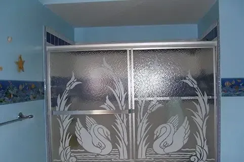 Shower with frosted glass doors featuring swan and plant design. Blue walls and trim.