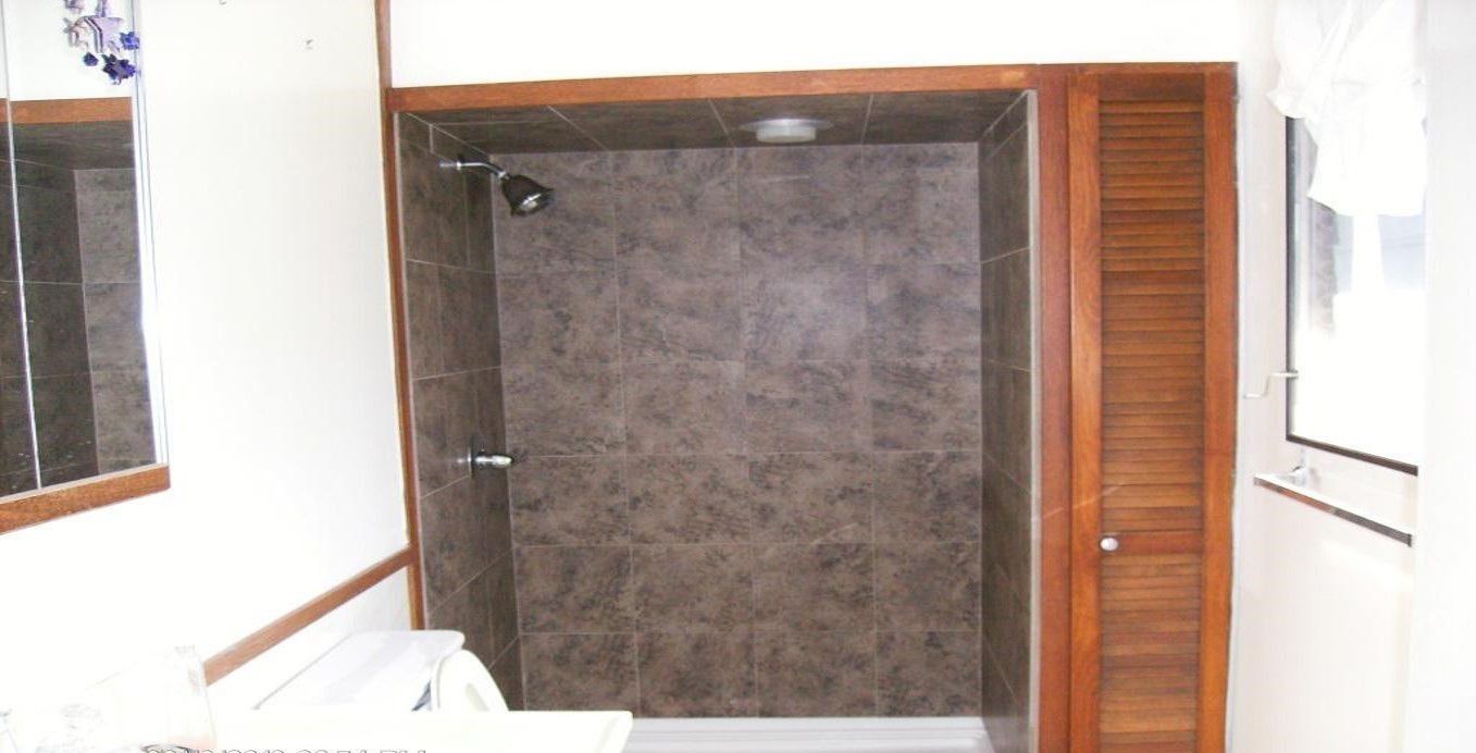 Brown-tiled shower with a showerhead in a bathroom. A wooden cabinet is on the right.