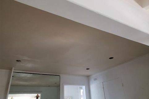 Ceiling with recessed lighting, freshly plastered in beige, and white trim.