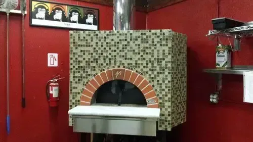 Pizza oven in a red-walled kitchen with a mosaic exterior, brick arch, and stainless steel features.