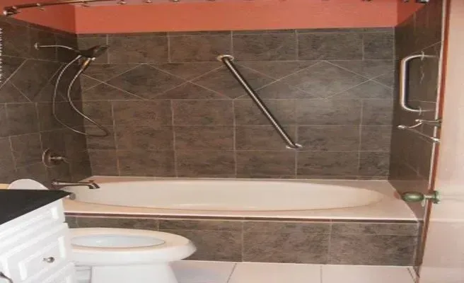 Bathroom with brown tile, white bathtub, grab bar, and toilet.