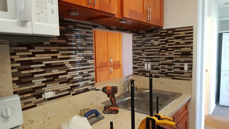 Kitchen backsplash installation in progress. Brown, tan, and white mosaic tiles. Tools on the countertop.