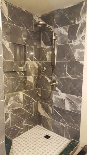 Dark gray marble-patterned tiled shower with built-in shelf and white patterned floor, silver fixtures.