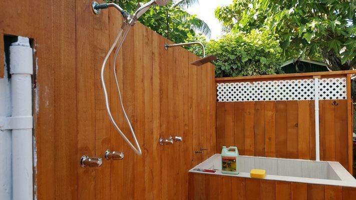 Outdoor wooden shower with multiple showerheads and a small tub.