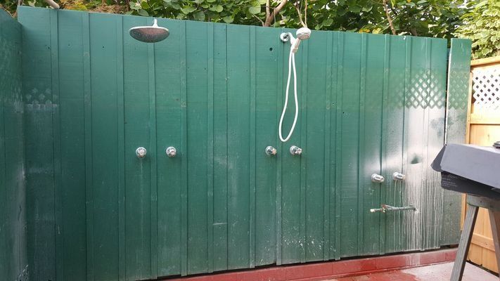 Green outdoor shower with multiple showerheads and controls.