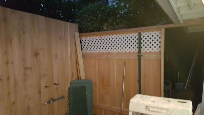 Wooden fence in a yard with latticework top, a green chair, and a white appliance.