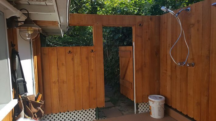 Outdoor wooden shower stall with open doorway and showerhead.