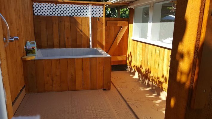 Outdoor bathtub and shower enclosed by wooden walls.
