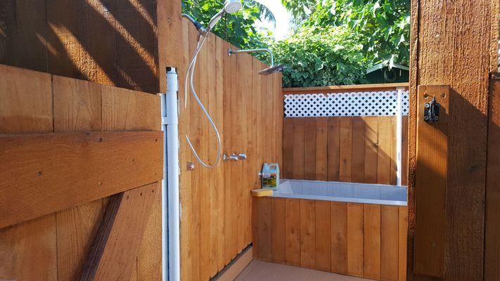 Outdoor shower with wooden walls, tub, and silver shower head.
