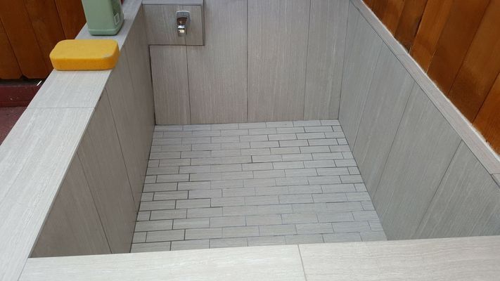 An empty, tiled shower stall with a yellow sponge and a faucet.