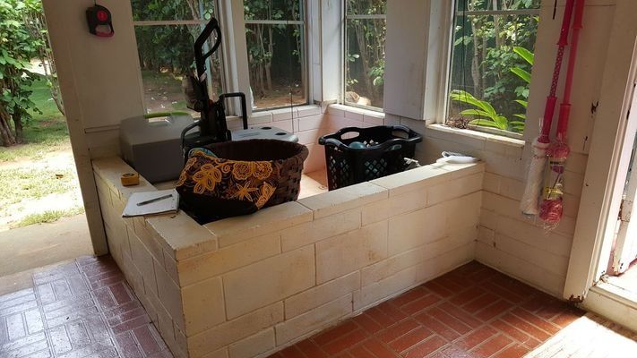 Enclosed outdoor laundry area with brick wall, brown tiled floor, and windows overlooking greenery.