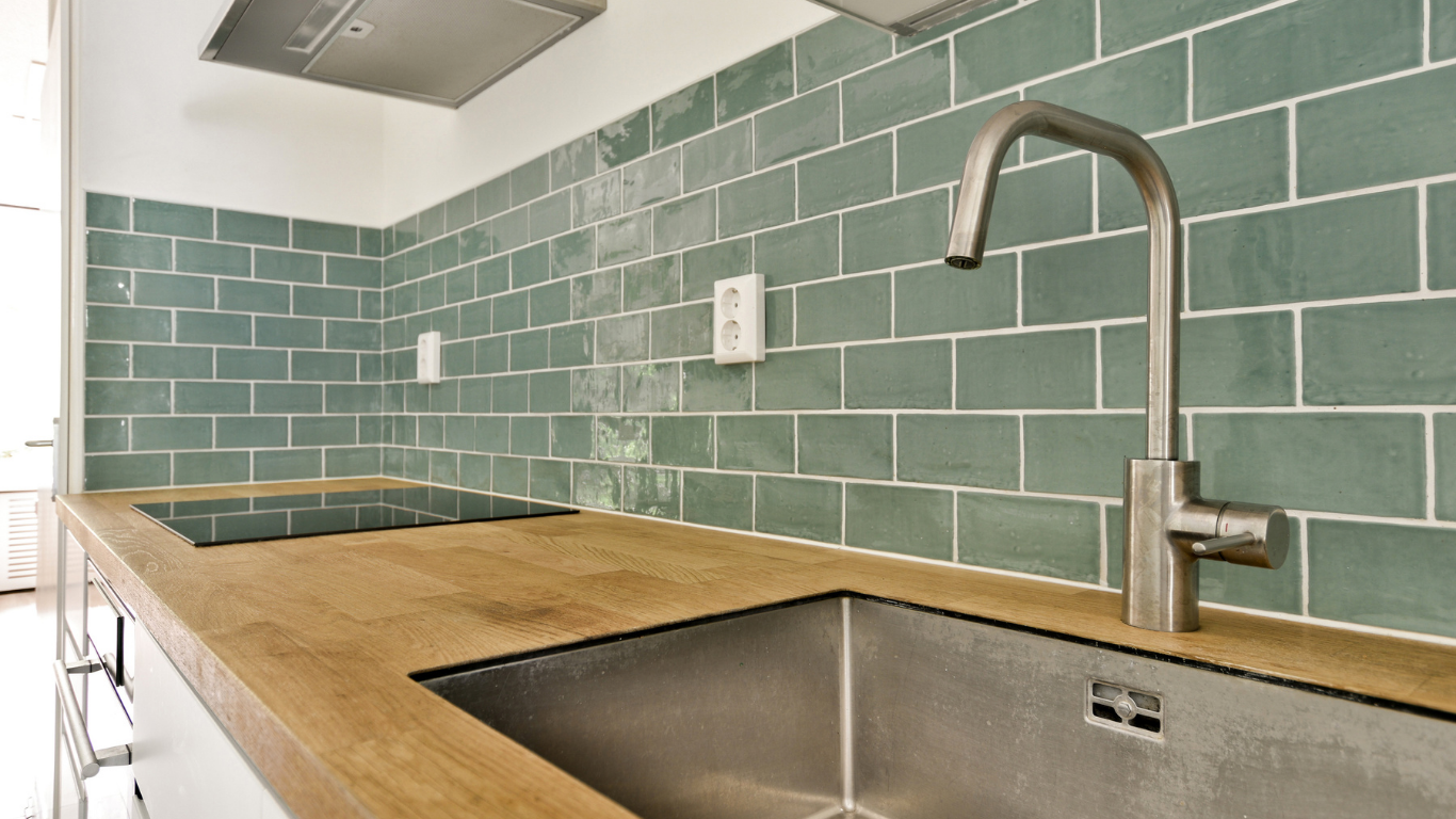 Kitchen with teal subway tile backsplash, wooden countertop, and stainless steel sink and faucet.