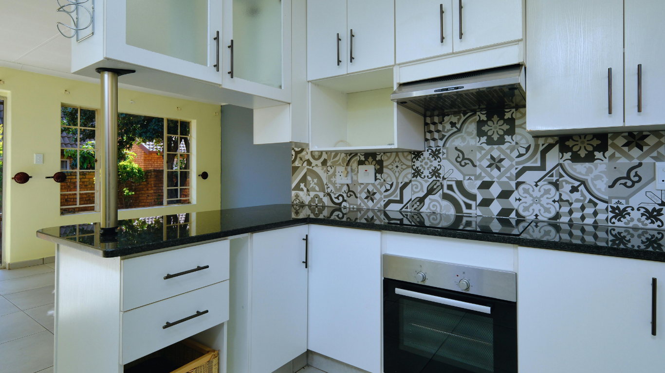 White kitchen with black countertops, oven, and patterned backsplash.