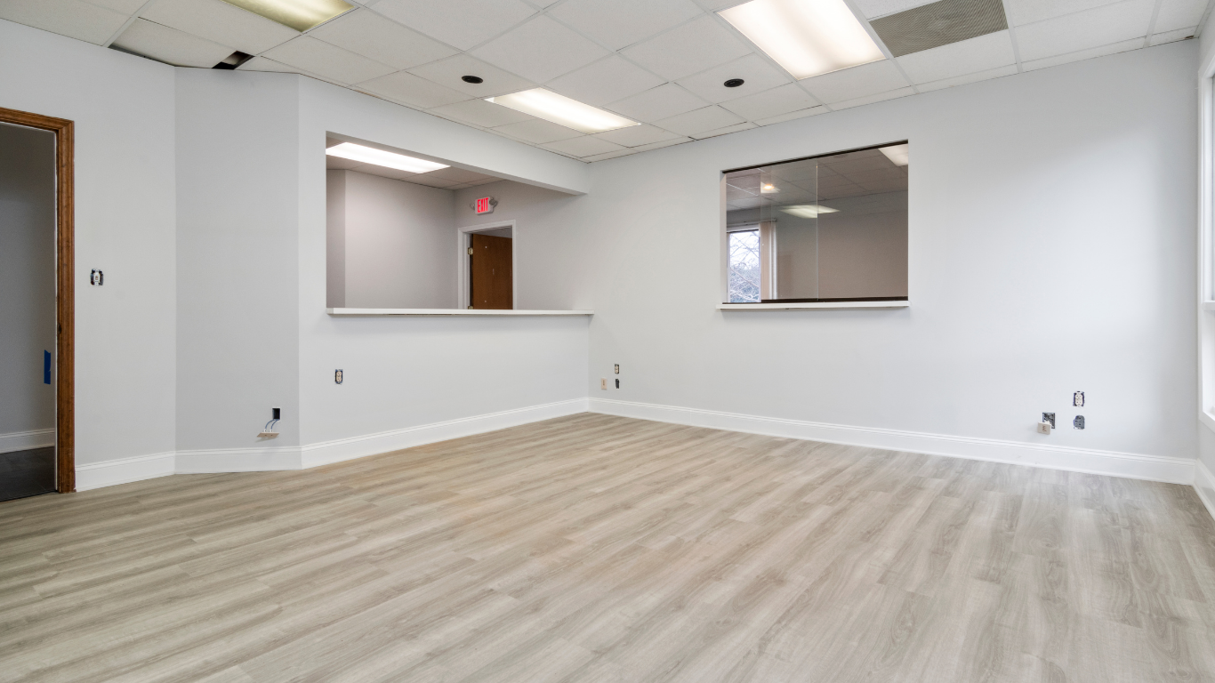 Empty office space with gray walls, light wood-look floor, and a service counter.